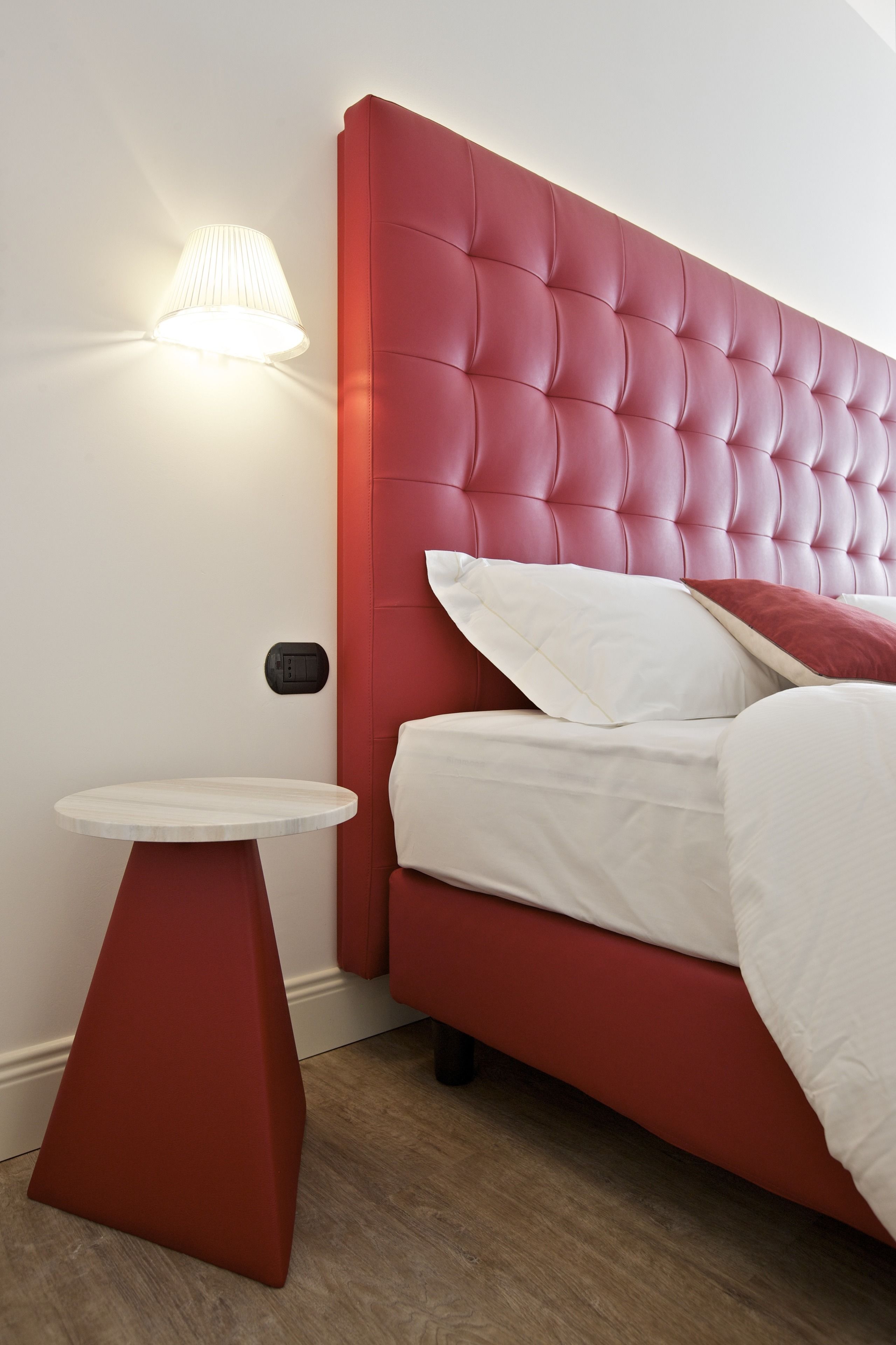 Una camera da letto moderna con una testiera imbottita rossa, un comodino rotondo e una lampada a parete.
