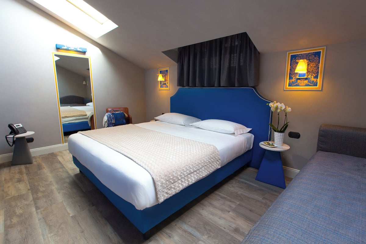 Ein modernes Hotelzimmer mit einem großen Bett, Nachttischen, einem Schreibtisch und einem Sessel.