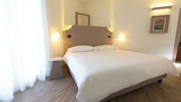 Una cama bien hecha en una habitación de hotel, con piso de madera, una mesita de noche y lámparas fijadas a la pared.
