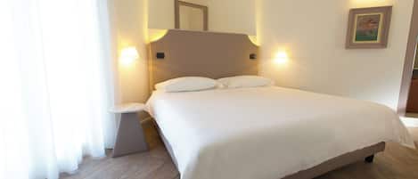 Un lit bien fait dans une chambre d’hôtel, avec un plancher en bois, une table de chevet et des lampes fixées au mur.