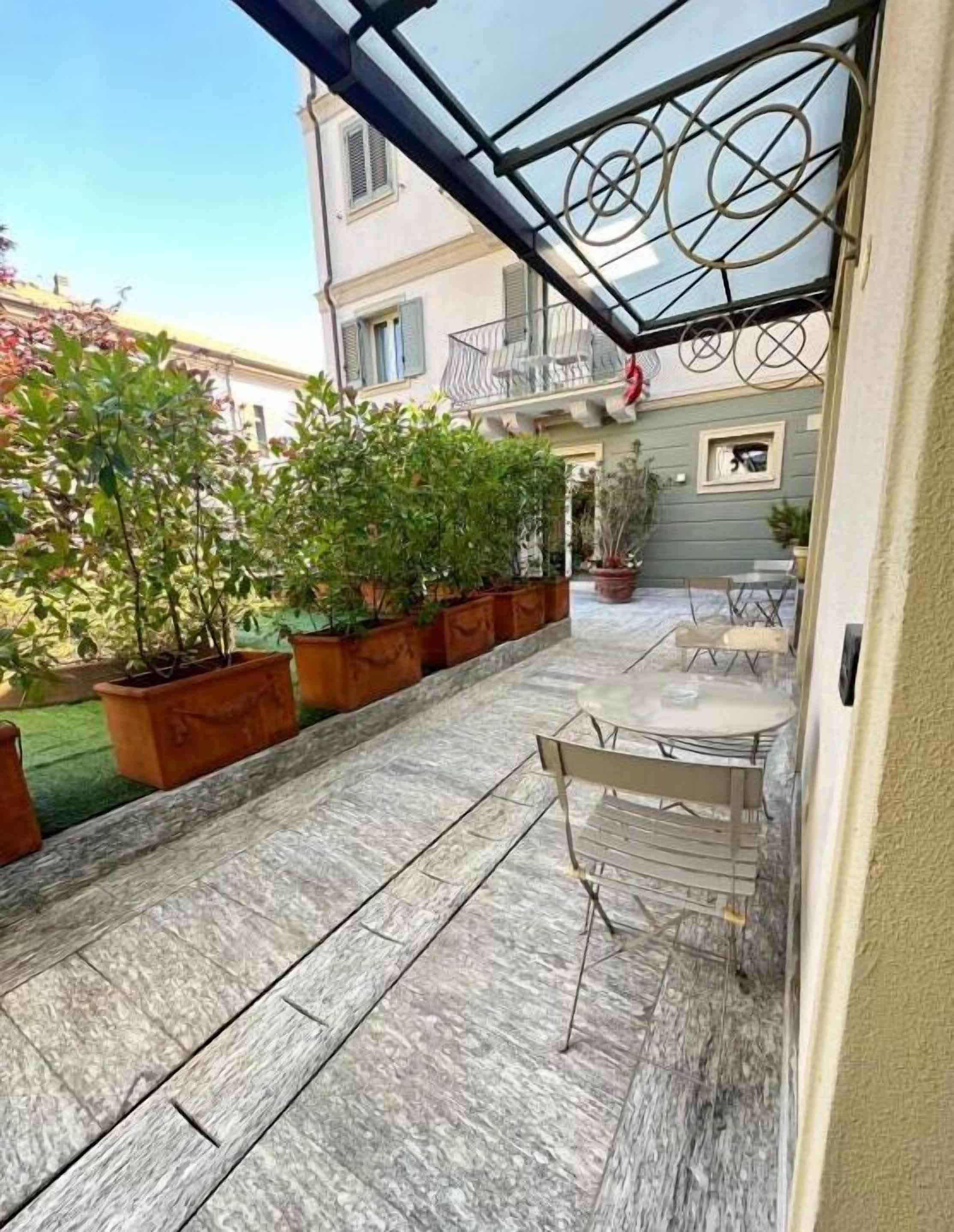 A covered patio area with potted plants, a seating area, and a view of a building with balconies.
