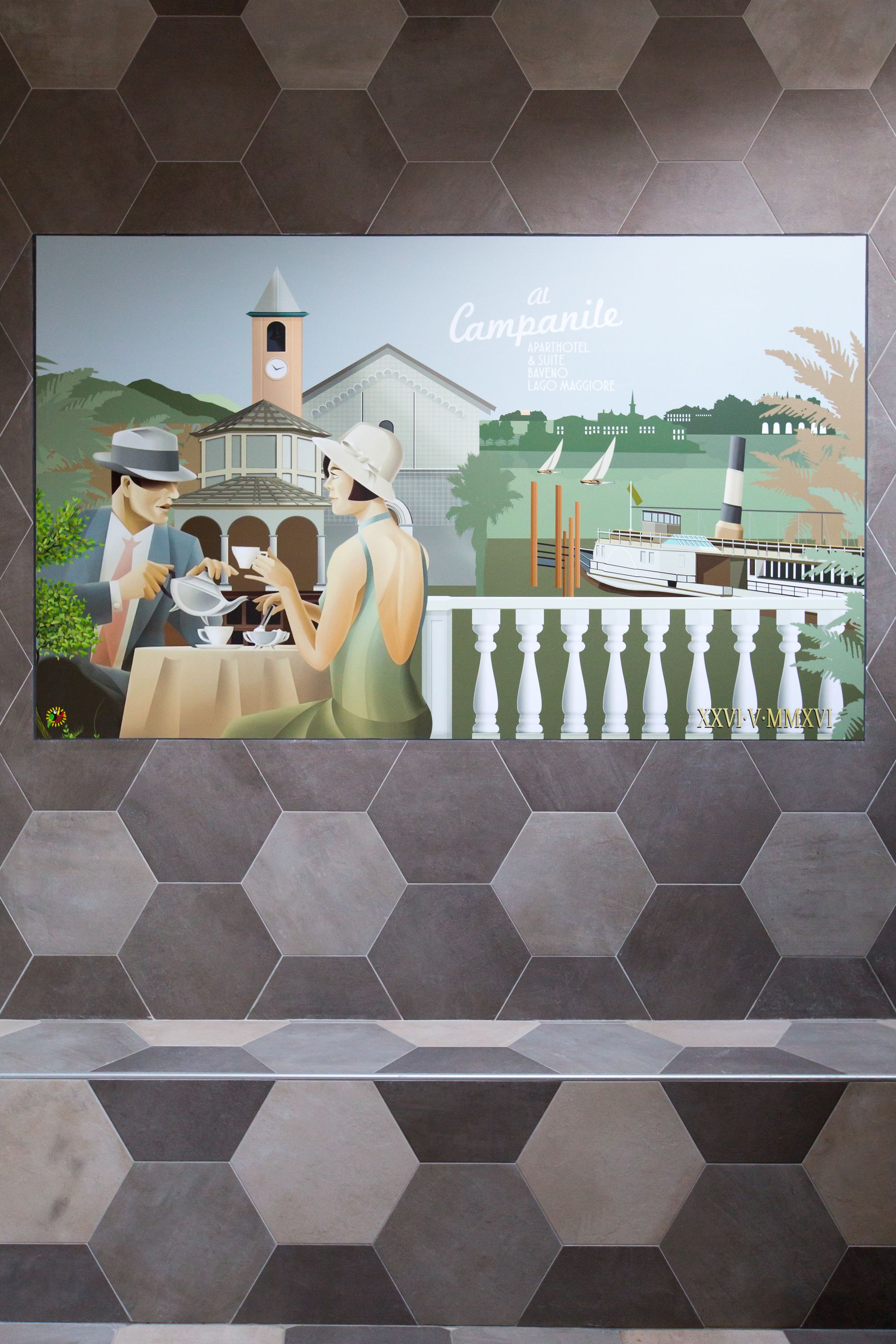 L’intérieur d’un hôtel présente des carreaux à motifs hexagonaux, une œuvre d’art encadrée représentant un couple à une table, et une vue sur un bateau et un phare.