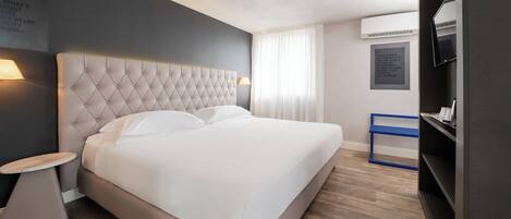 A modern hotel room with a large bed, a bedside table, a TV, and a wall-mounted air conditioner.
