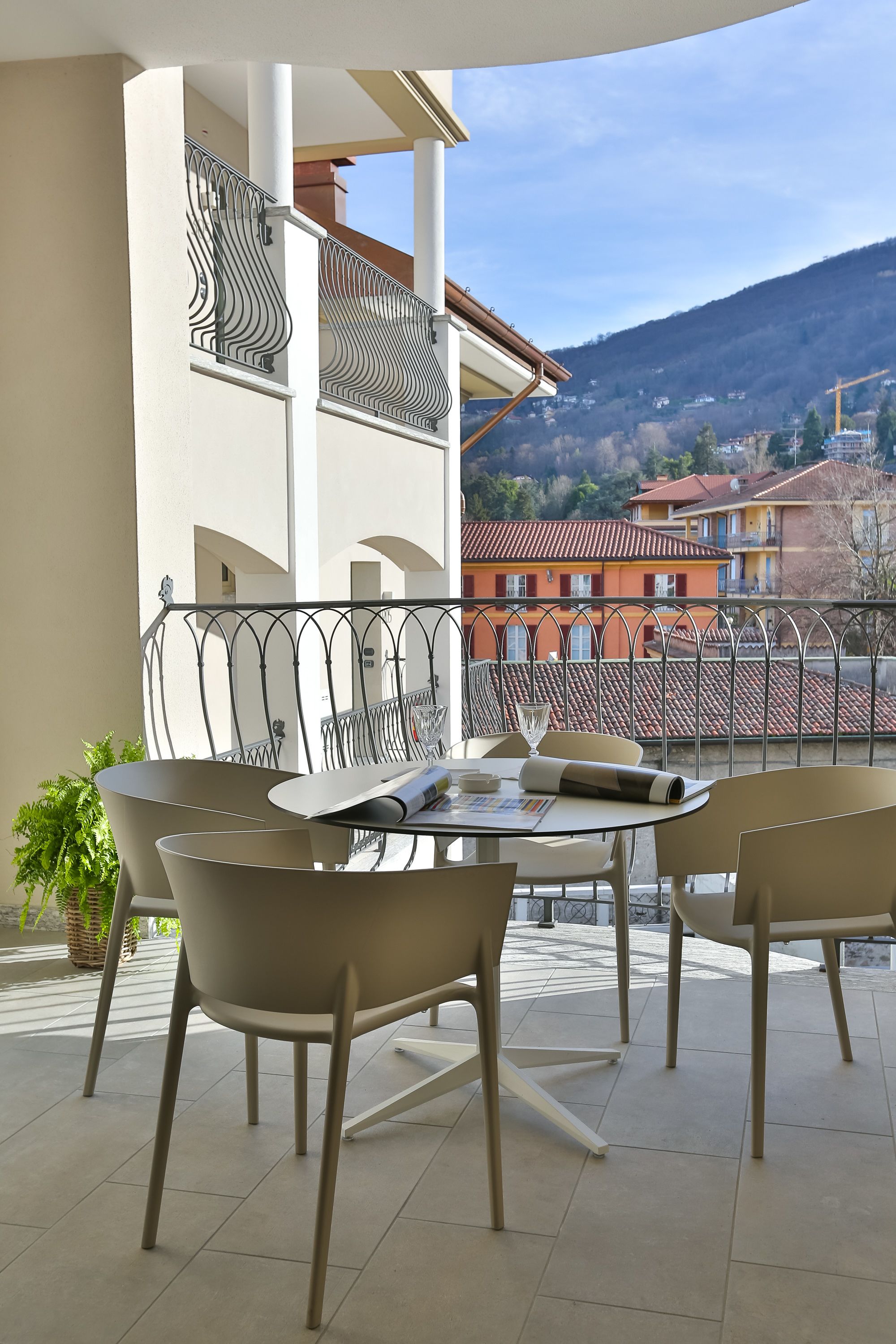 Un balcon avec une table et des chaises, un pot de fleurs et une vue sur des immeubles et des collines.