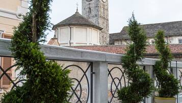 A balcony with potted plants and a clock tower in the background.
