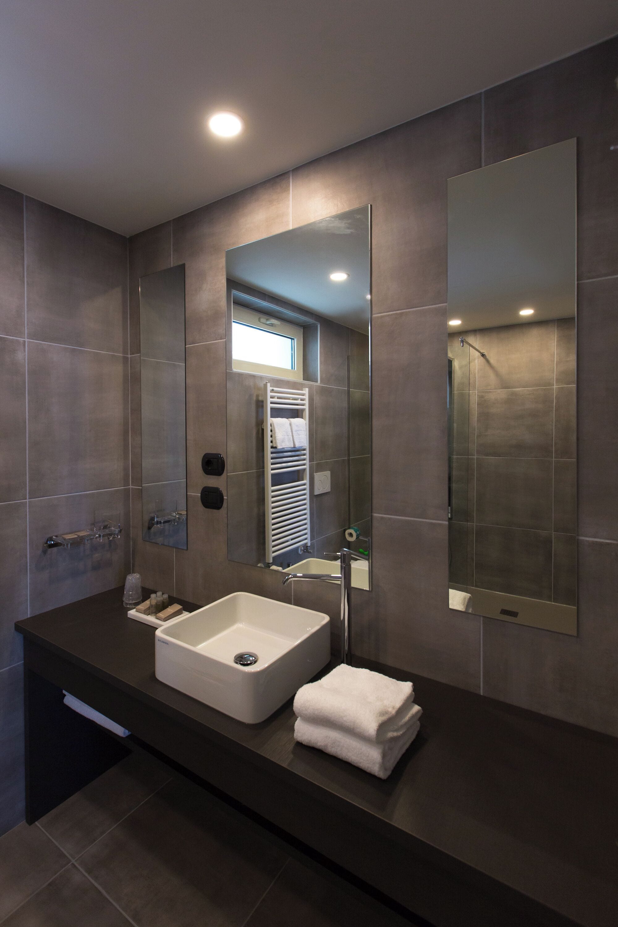 A modern bathroom with a large mirror, a white sink, and a towel on the counter.