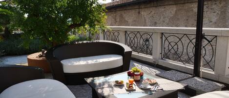 Um pátio com móveis de vime, uma mesa posta para o café da manhã e vista para um edifício com torre.