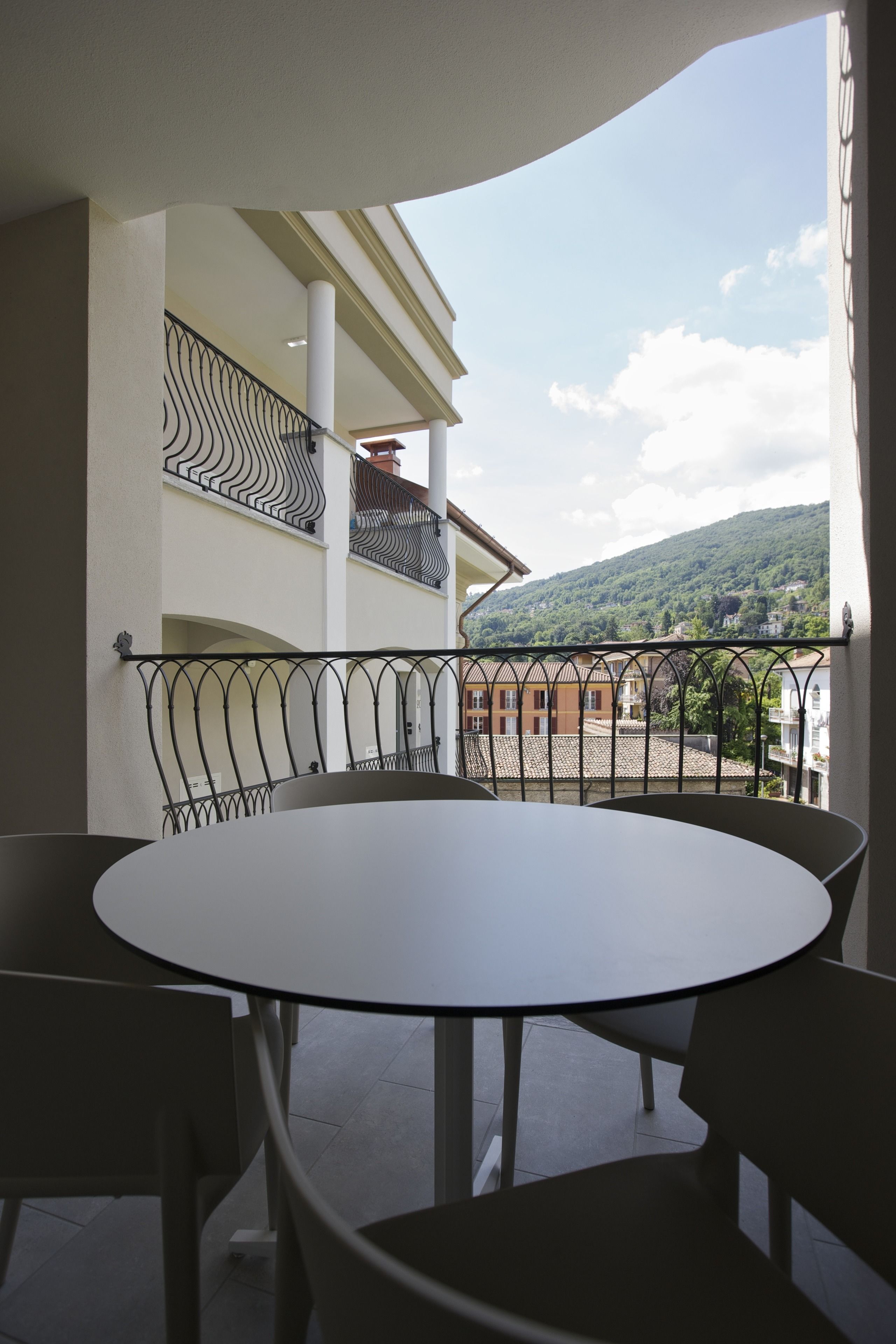 Un balcon avec une table ronde et des chaises, une rambarde en métal, et une vue sur des bâtiments et une colline en arrière-plan.