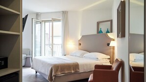 Quarto de hotel com cama, poltrona, televisão e varanda com guarda-corrimão.