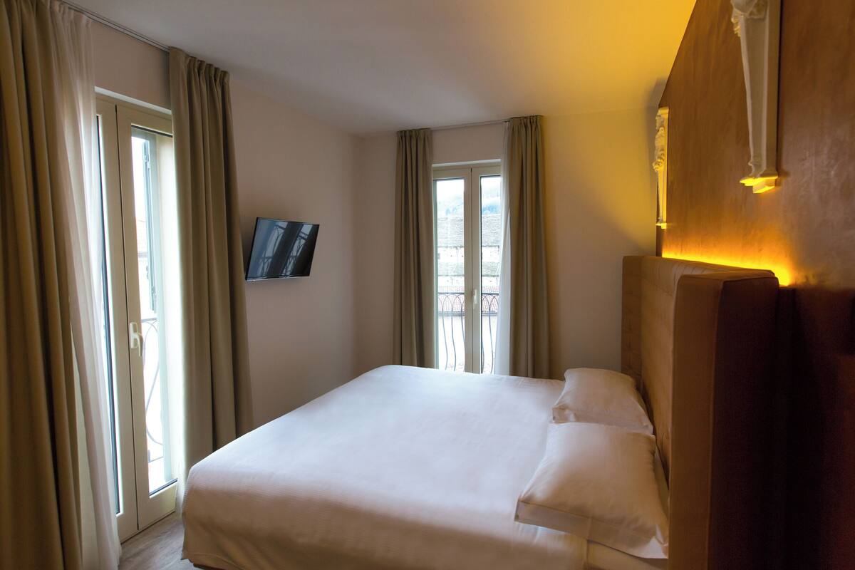 Ein Hotelzimmer mit einem großen Bett, einem an der Wand befestigten Fernseher und einem Fenster mit Vorhängen.