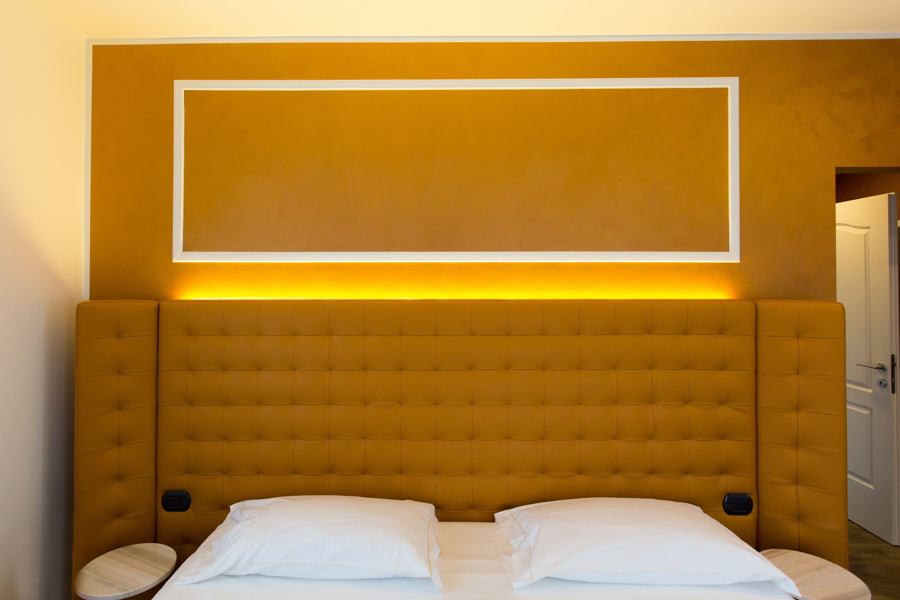 A room with a large, tufted headboard, a bed with white linens, and a wall-mounted light fixture.