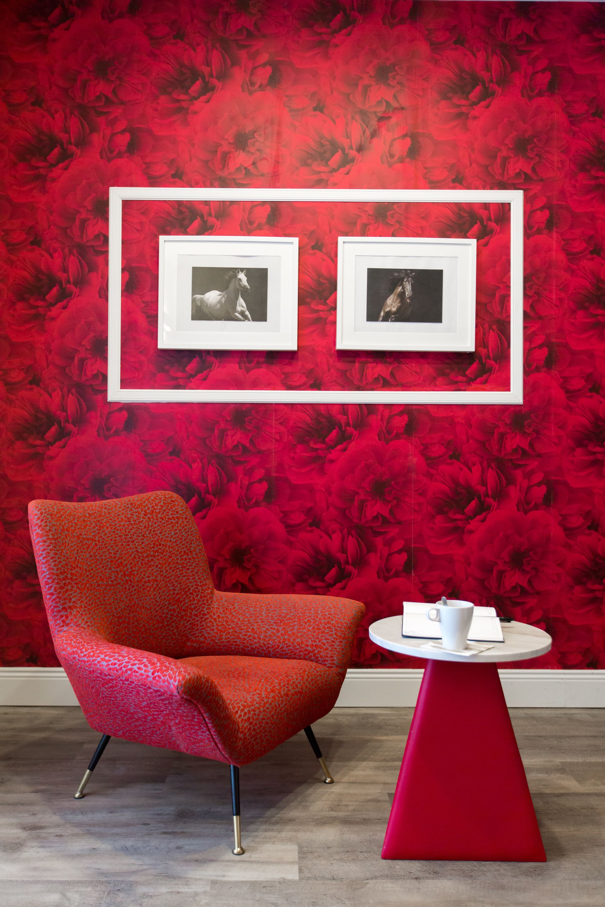 Un papier peint à motifs floraux rouges, un fauteuil rouge et deux tableaux encadrés accrochés au mur.