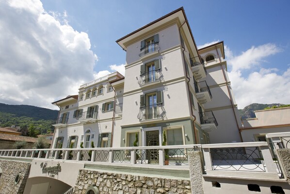 A multi-story hotel with balconies, a stone facade, and a mountainous backdrop. - Hotel Al Campanile - Luxury Suites & Apartments (Baveno)