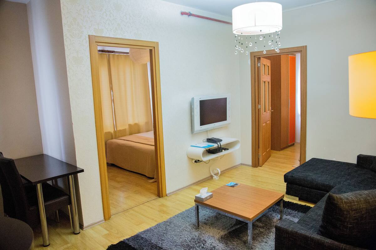 A compact living space with a wooden table, a sofa, a TV mounted on the wall, and a door leading to another room.