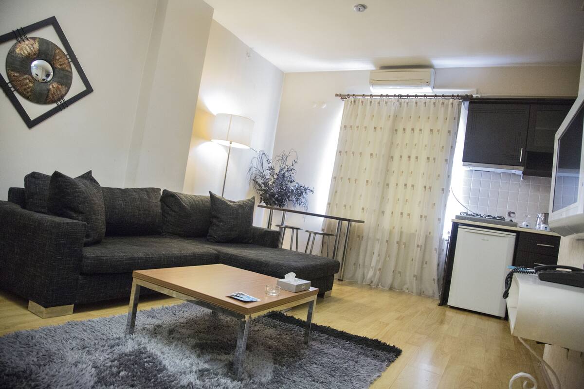 A living room with a sofa, a coffee table, and a small kitchen area with a refrigerator and a sink.