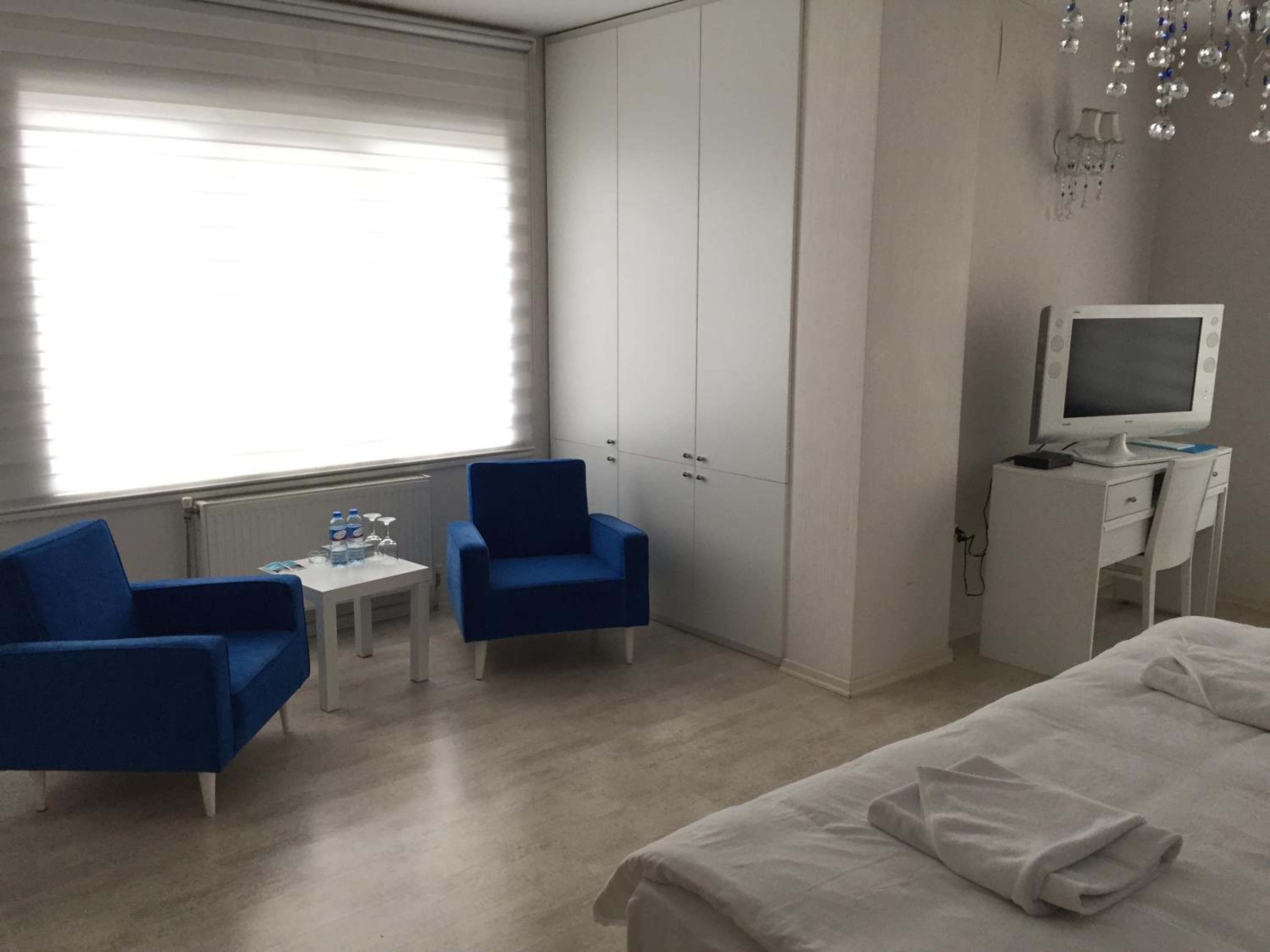 Habitación de hotel con cama, escritorio con computadora, dos sillas azules, una mesita con botellas de agua y un armario.