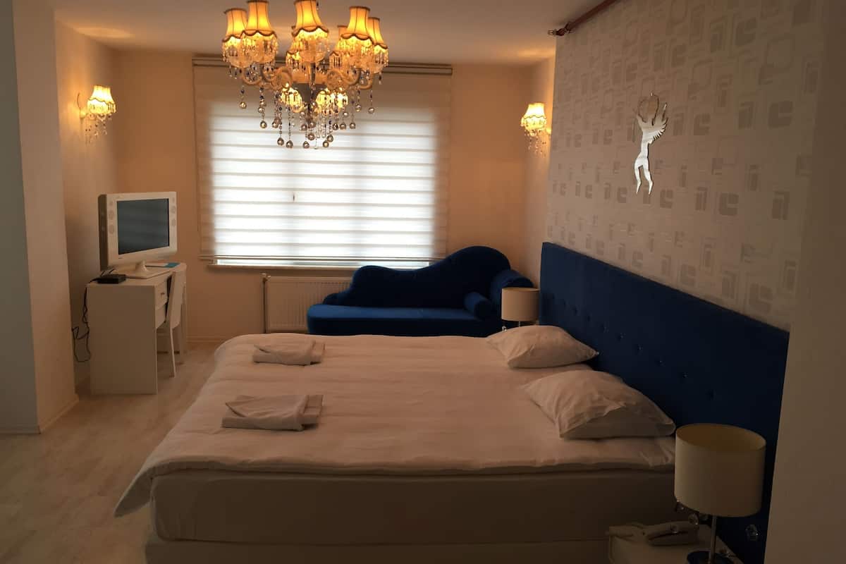 A bedroom with a large bed, a desk with a computer, a blue sofa, a chandelier, and a wall with a decorative animal.