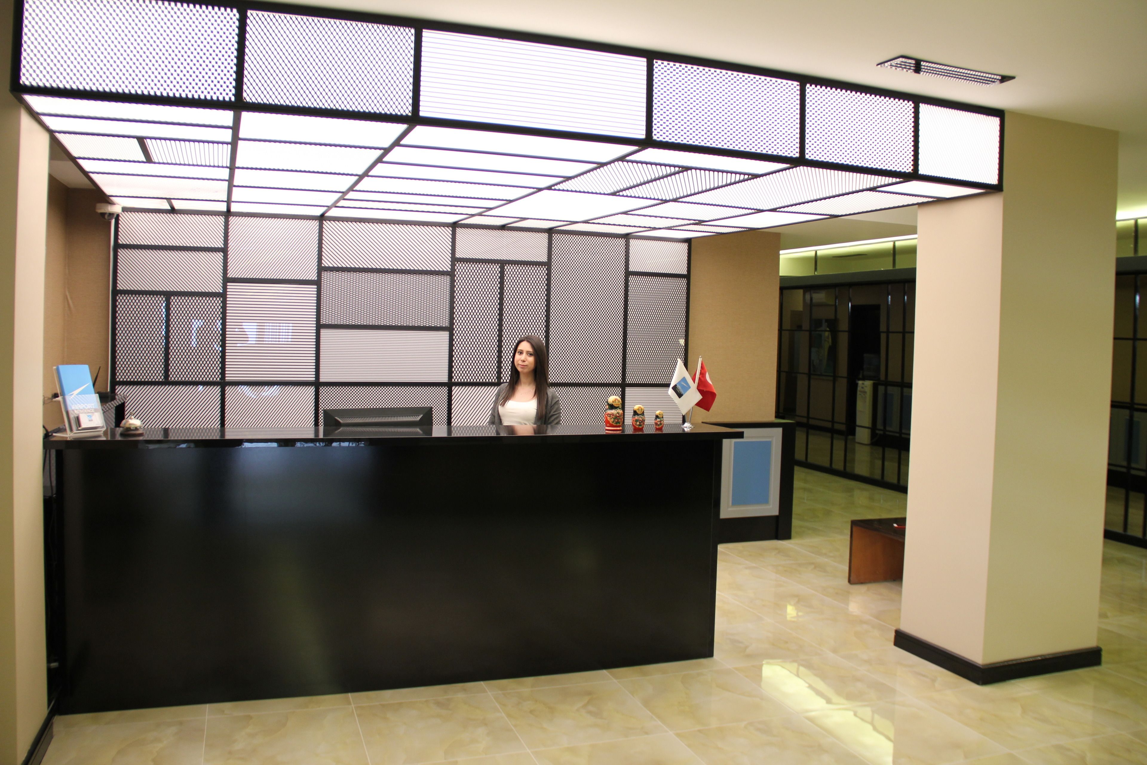 A reception desk with a modern design, a person standing behind it, and a patterned wall in the background.