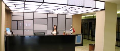 A reception desk with a modern design, a person standing behind it, and a patterned wall in the background.