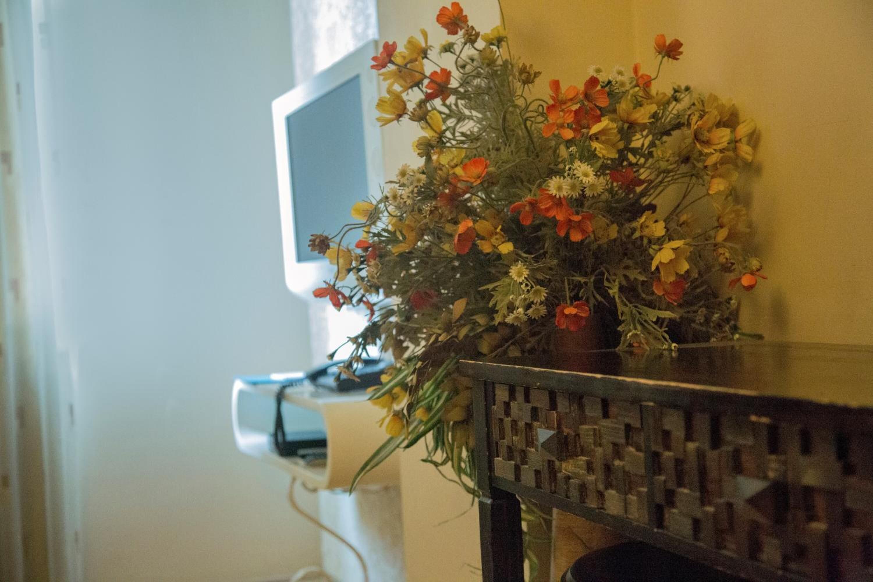 A desk with a vase of flowers and a computer monitor.