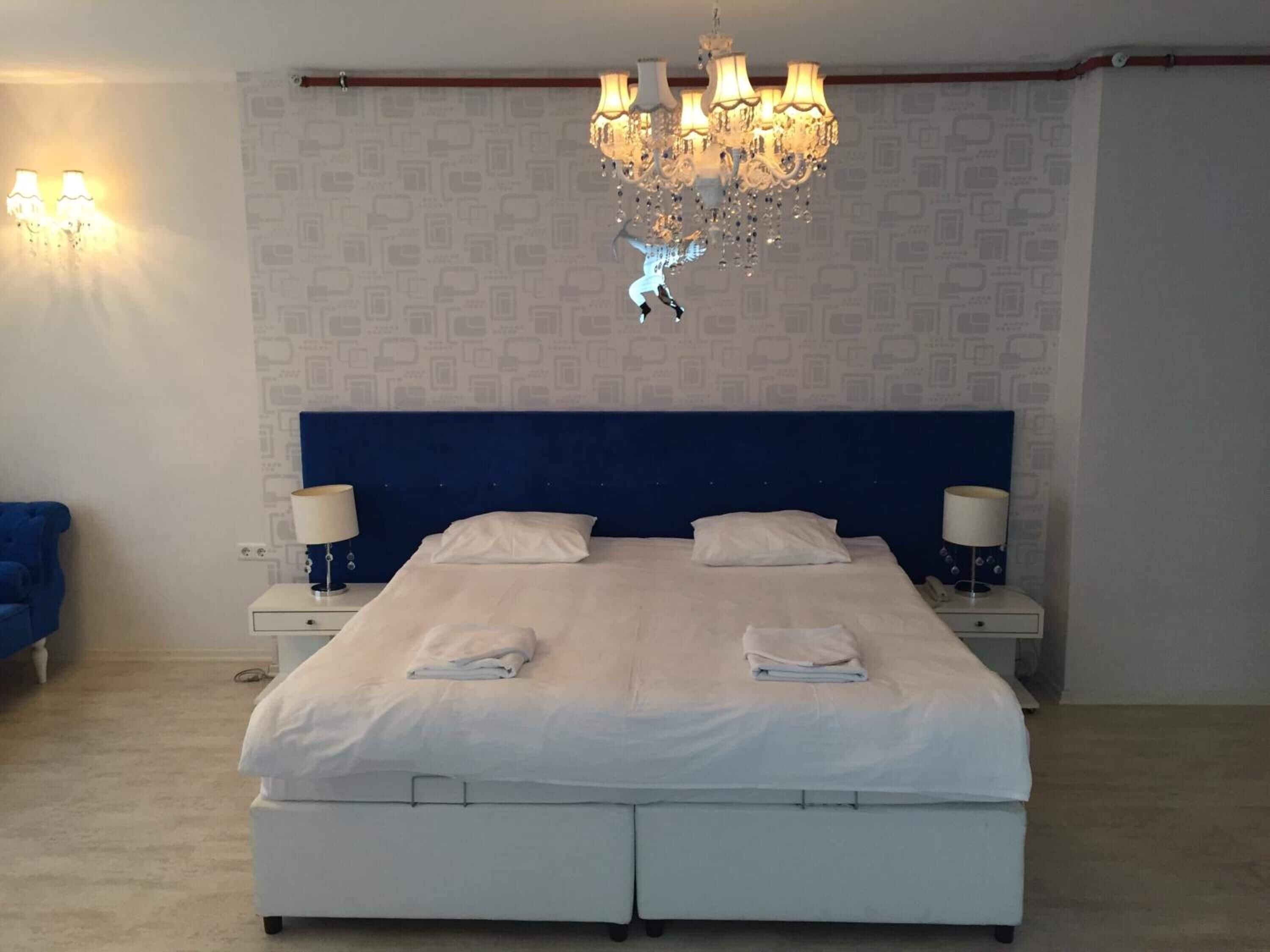 A bedroom with a double bed, two bedside tables with lamps, a chandelier, and a patterned wallpaper.