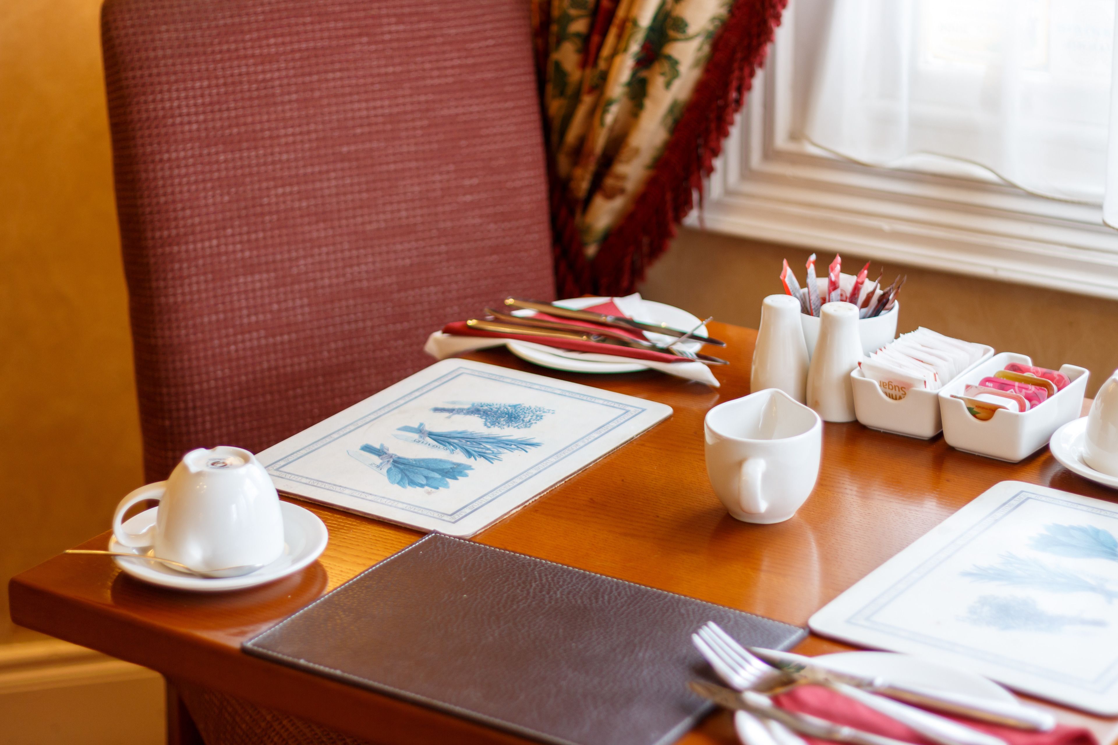 A neatly arranged dining table with a white cup, saucer, and a set of cutlery.