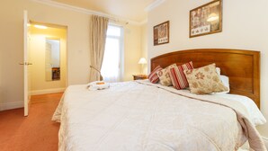 Una cama bien tendida con un cabecero de madera, una mesita de noche con lámpara y dos cuadros enmarcados en la pared.