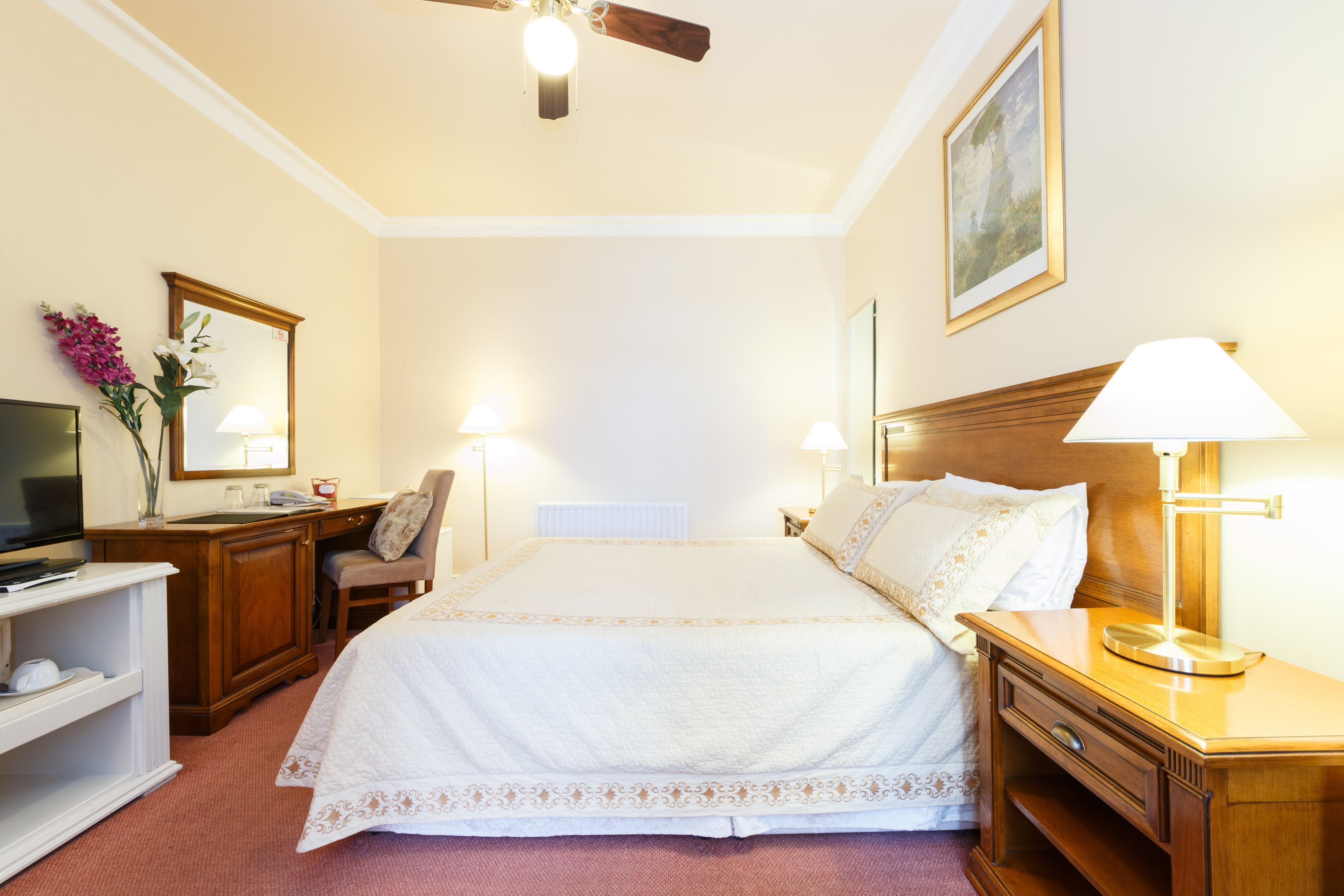 A hotel room with a bed, bedside tables, a TV, a desk, and a chair.