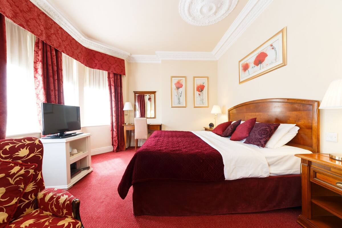 A hotel room with a large bed, a television on a stand, a desk with a chair, and artwork on the walls.