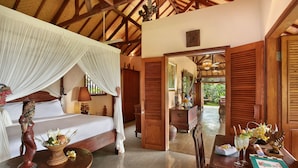 A bedroom with a canopy bed, wooden furniture, and a view of the garden through an open door. - Villa Patria (Sukasada)