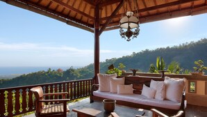 A wooden deck with a sofa and chairs, overlooking a mountainous landscape. - Villa Patria (Sukasada)