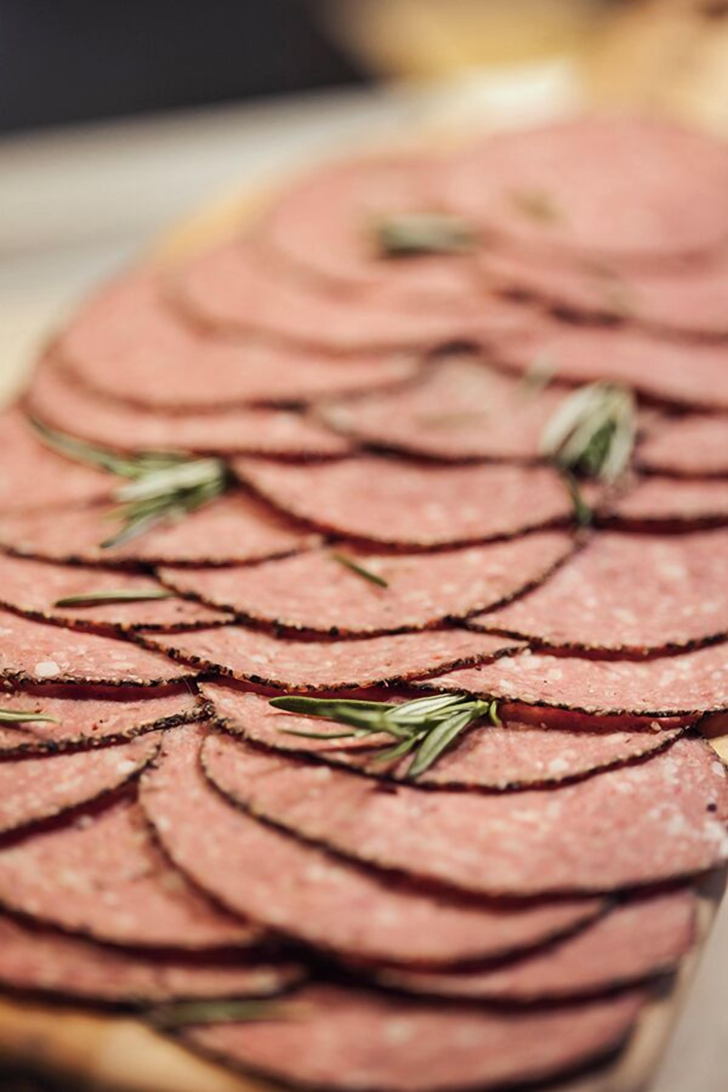 A close-up of thinly sliced meat arranged in a circular pattern, garnished with rosemary sprigs.