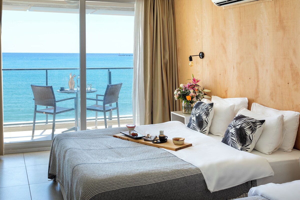 A hotel room with a bed, a breakfast tray, a table with chairs, and a view of the sea.