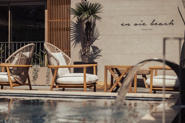 Zona de piscina con sillas de mimbre y una pared con el texto "en vie beach since 2015".
