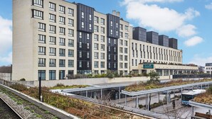 A modern hotel with multiple floors, a covered outdoor area, and a bus stop. - Appart'hôtel Odalys City Campus - Paris Rueil Malmaison (Rueil-Malmaison)