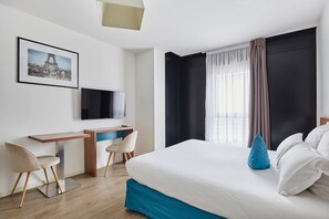 A modern hotel room with a large bed, a desk with a chair, a television, and a picture of the Eiffel Tower on the wall.