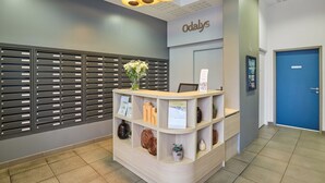 A reception desk with a nameplate, a blue door, and a wall-mounted security camera. - Appart'hôtel Odalys City Campus - Paris Rueil Malmaison (Rueil-Malmaison)