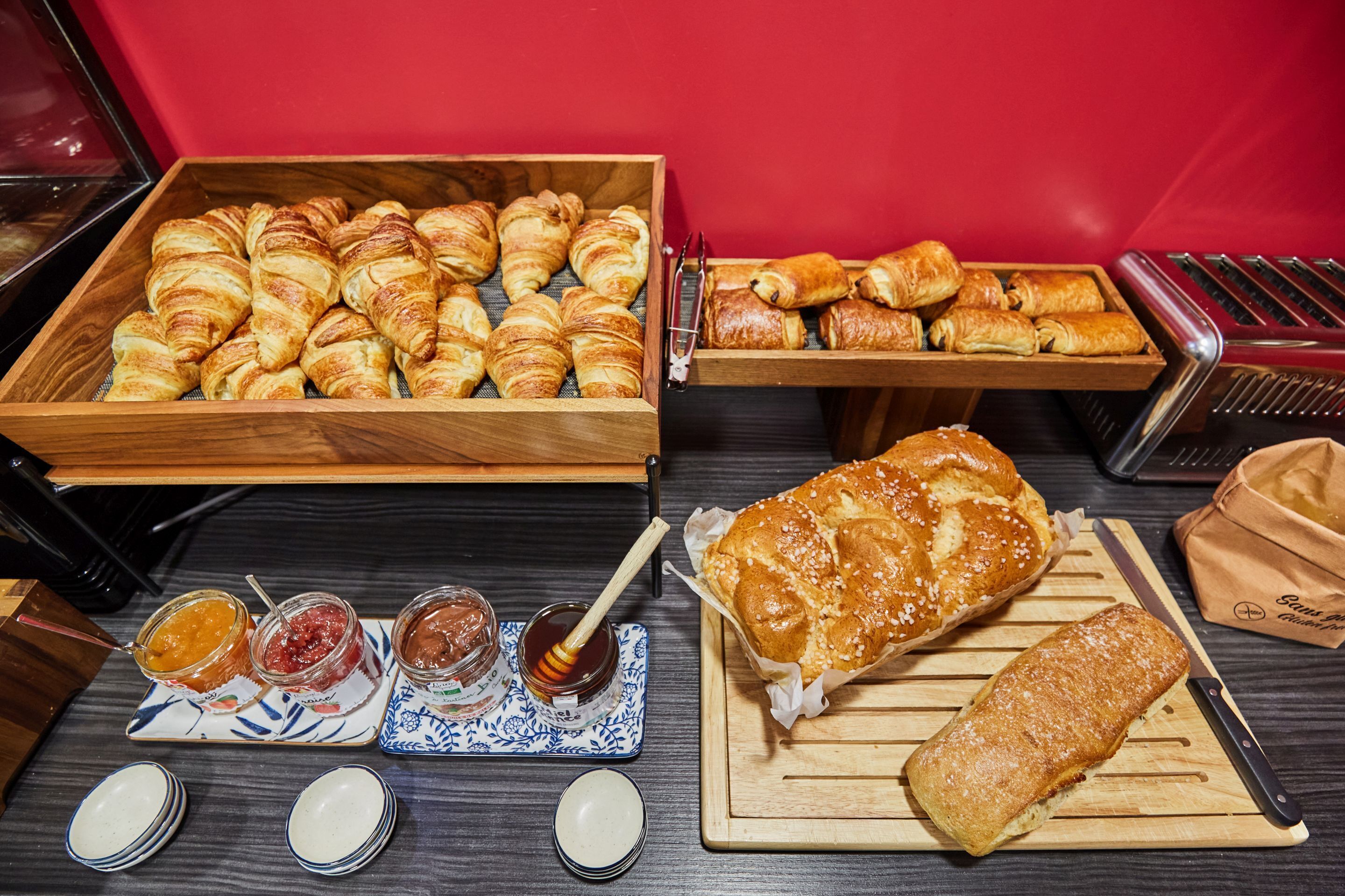 A variety of pastries and bread on display, including croissants, a baguette, and a loaf of bread on a wooden cutting board.