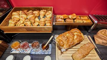A variety of pastries and bread on display, including croissants, a baguette, and a loaf of bread on a wooden cutting board.