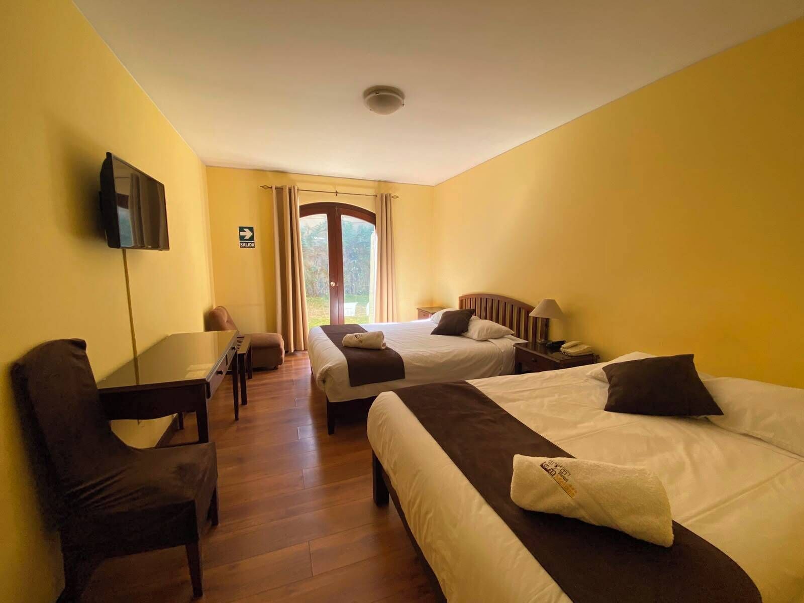 A hotel room with two beds, a desk, a chair, a television, and a view of the outdoors.