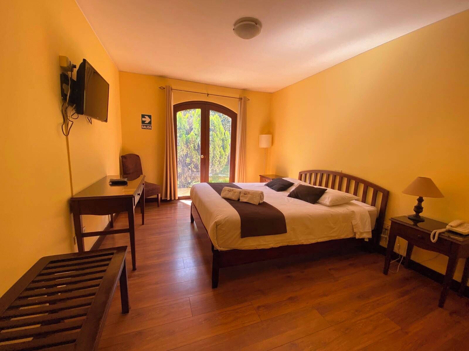 A hotel room with a bed, a desk, a chair, a television, a telephone, and a window with curtains.