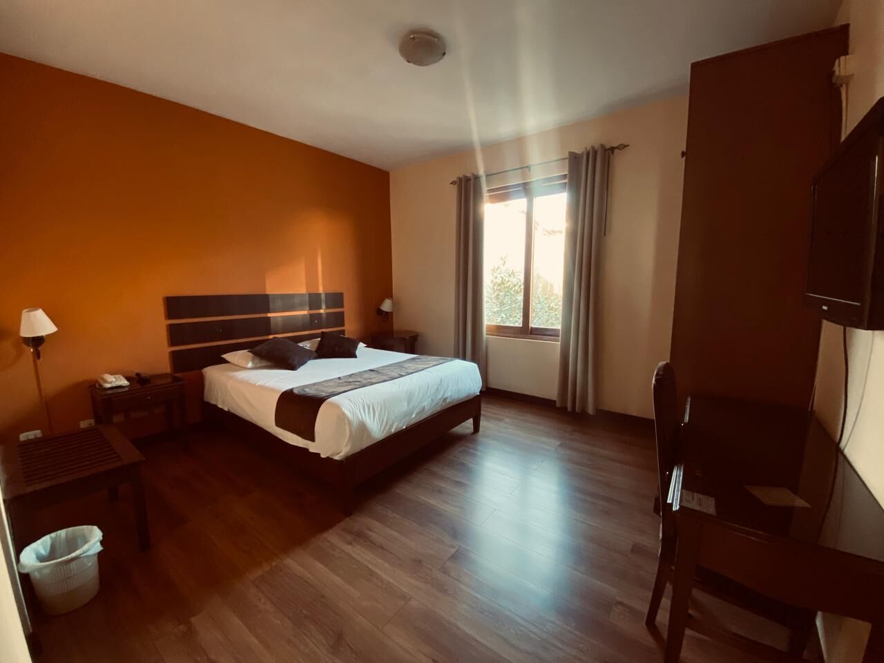 A hotel room with a bed, bedside tables, a chair, a desk, and a window with curtains.