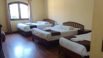 Una habitación con tres camas de madera, una ventana con cortinas y piso de madera.