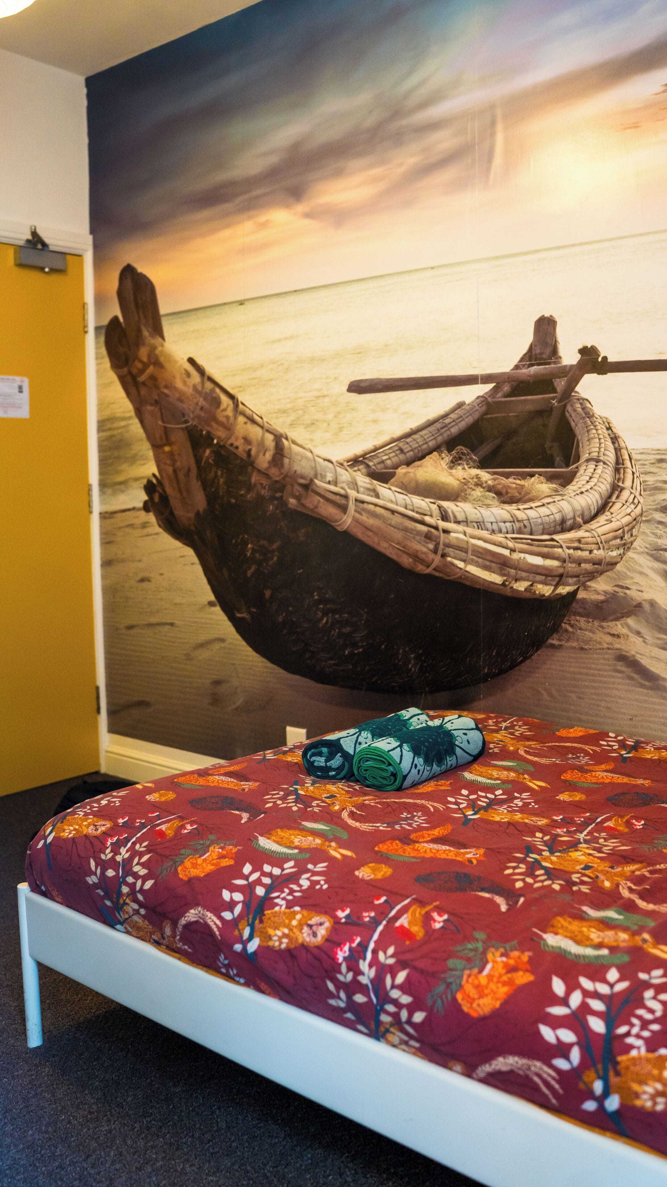 Una cama con una colcha floral, una pared con un cuadro de un barco y una pared amarilla.