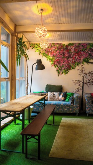 A cozy room with a wooden table, bench, sofa, and a decorative wall with a floral pattern. - Igloo Hybrid - Hostel (Nottingham)
