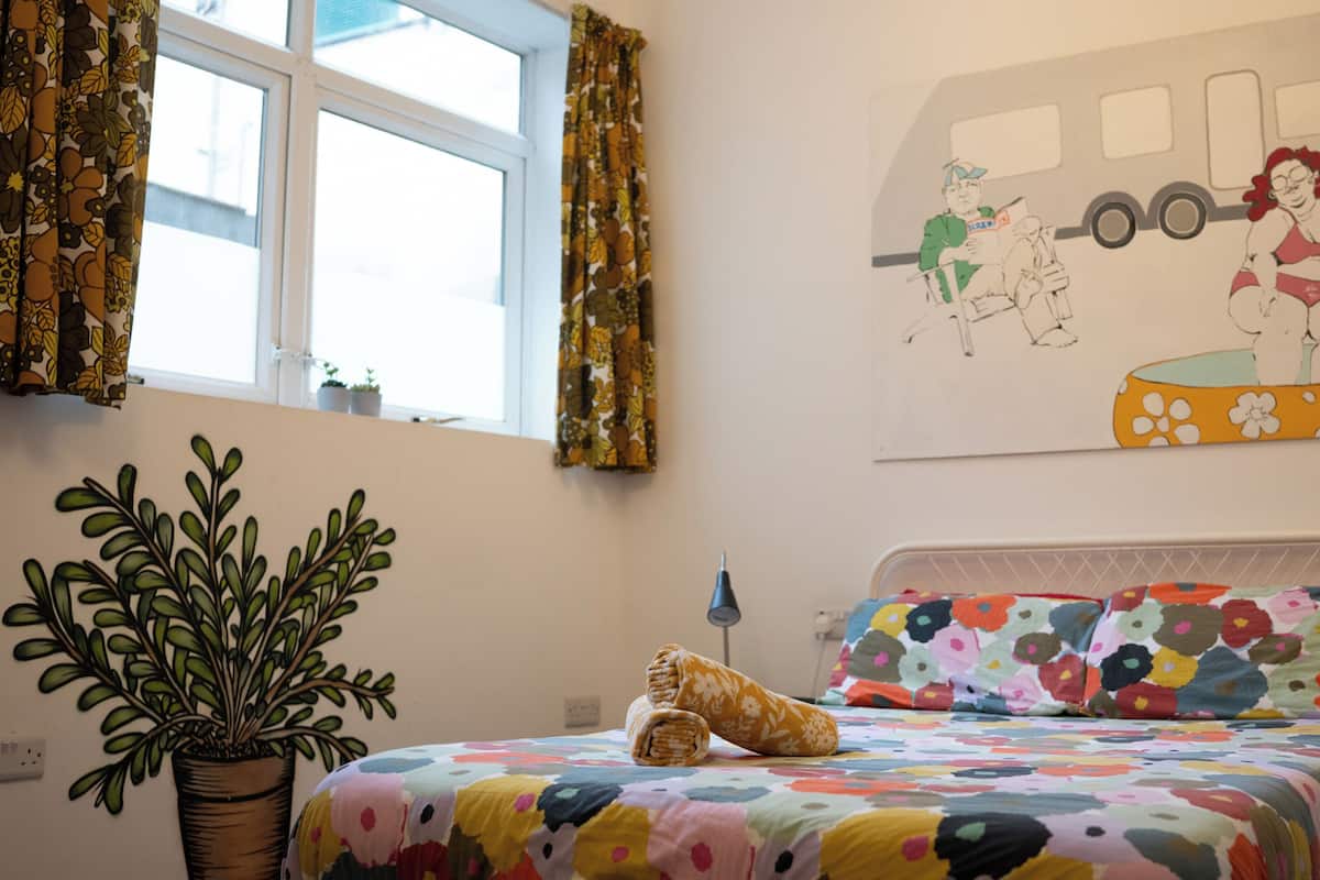 A bedroom with a bed, a potted plant, a wall painting, and a window with curtains.