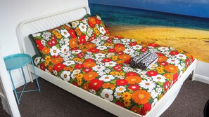 A bed with a floral bedspread, a blue side table, and a beach mural on the wall. - Igloo Hybrid - Hostel (Nottingham)