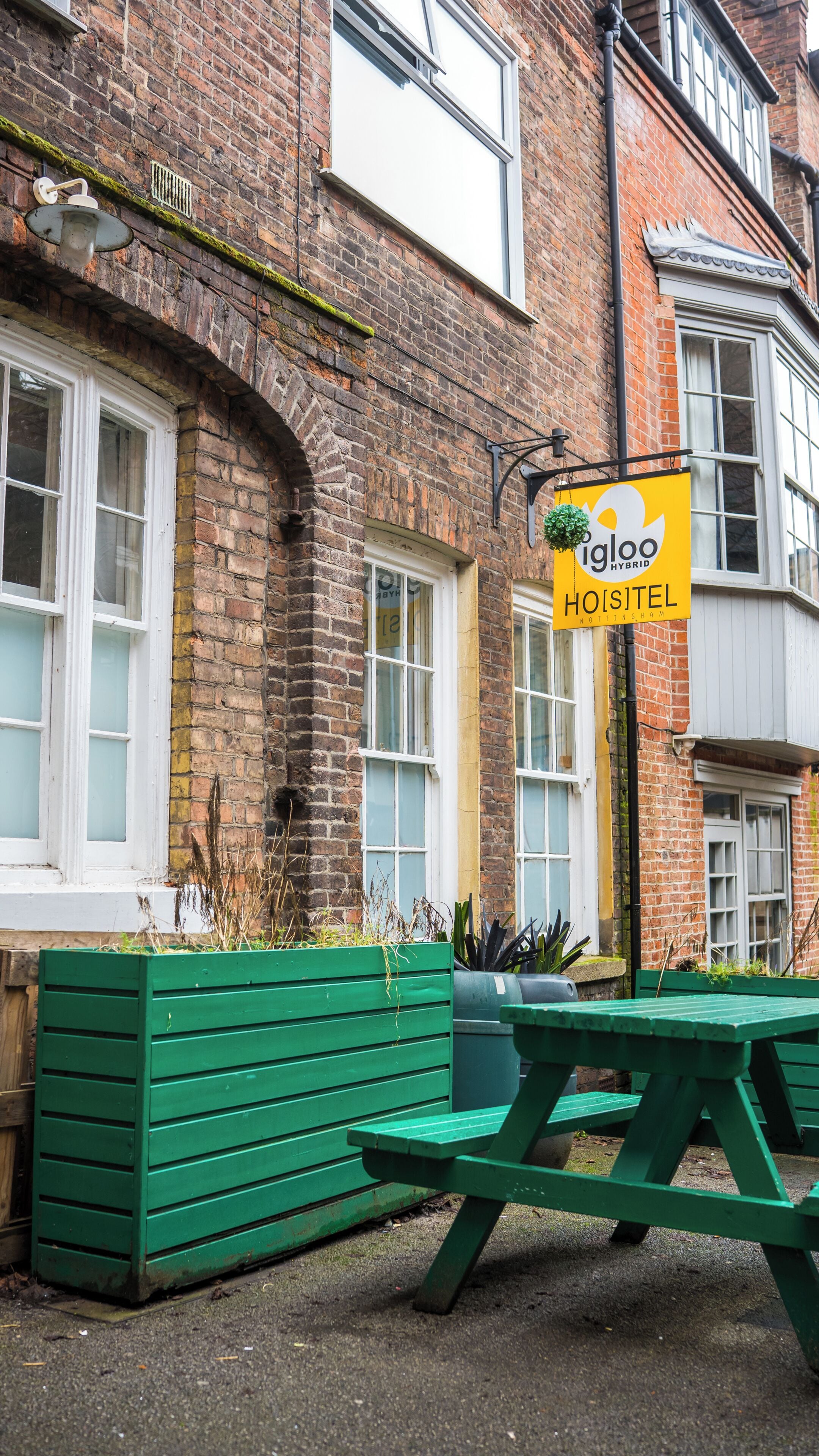 A brick building with a sign for 'igloo hybrid hotel' and a green outdoor seating area.