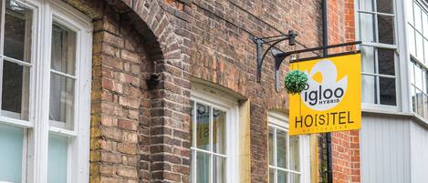A brick building with a sign for 'igloo hybrid hotel' and a green outdoor seating area.