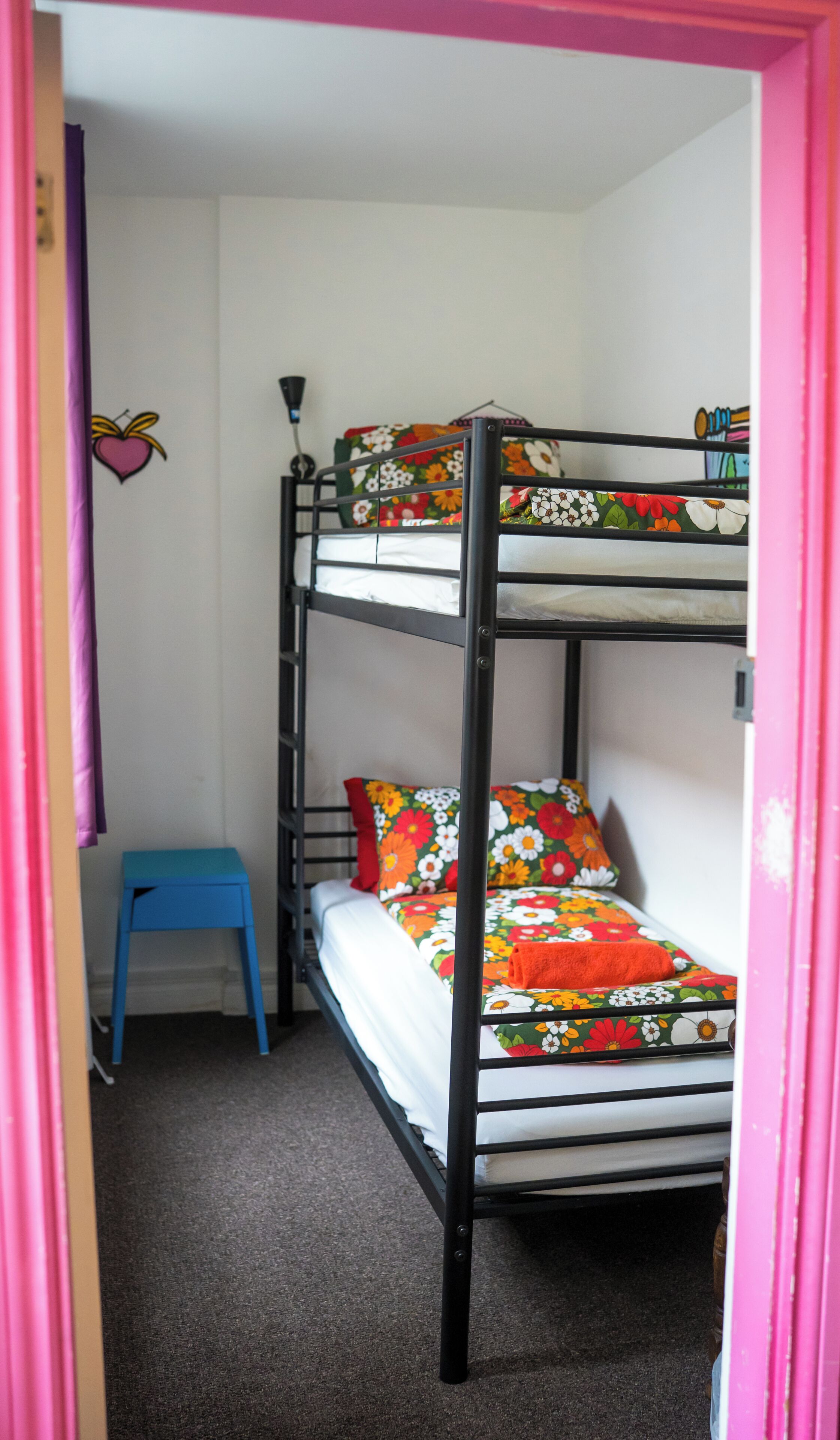 Una cama litera con ropa de cama floral, un taburete pequeño azul y una pared decorada con un corazón.